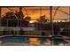 Backyard pool with a screened-in enclosure reflects a beautiful sunset in a private backyard at 1313 Key West Ct, Wesley Chapel, FL 33544