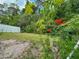 Green backyard with a white fence, various plants and flowers, and overgrown lawn at 2349 Wood Pointe Dr, Holiday, FL 34691