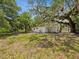 Backyard view with a glimpse of the compact white home, showcasing its surrounding lush greenery and mature trees at 7813 Cadillac Ave, Hudson, FL 34667