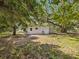 View of the home's backyard featuring a compact white home with mini-split units, lush greenery, and mature trees at 7813 Cadillac Ave, Hudson, FL 34667