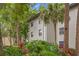 Side angle of a condo building featuring well-kept landscaping with tropical plants and tall palm trees at 3399 Mermoor Dr # 301, Palm Harbor, FL 34685