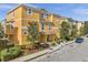 Bright yellow townhome featuring a neatly landscaped yard, decorative trees, and a well-maintained sidewalk at 456 Bayou Village Dr, Tarpon Springs, FL 34689