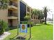 Condo exterior with lush lawn, palm trees and sign stating 