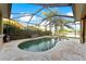 Screened-in pool area featuring travertine pavers, a lagoon-style pool with spa, and a lake view at 15104 Azra Dr, Odessa, FL 33556