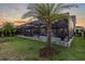 An outdoor screened-in pool with lounge chairs and umbrellas with nice lighting is set against a sunset backdrop at 3850 Bonfire Dr, Odessa, FL 33556