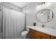Bathroom showcases a wood vanity, round mirror, tiled shower with curtain, and white flooring at 12705 Green Heron Way, Odessa, FL 33556