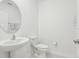 Clean half bathroom featuring a pedestal sink, a round mirror, a toilet and white walls at 6398 Bar S Bar Trl, Zephyrhills, FL 33541