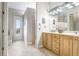 Bathroom with double vanity, wood cabinets, neutral tile floors, and access to the backyard at 2502 Fritzke Rd, Dover, FL 33527