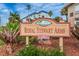 Royal Stewart Arms sign indicating a 55+ community with lush landscaping and palm trees at 8 Glencoe Pl # 305, Dunedin, FL 34698