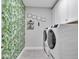 Bright laundry room featuring a modern washer and dryer, decorative wallpaper, shelving and framed artwork at 17845 Cortes Creek Blvd, Spring Hill, FL 34610