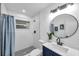 Bathroom with tiled shower, navy vanity, round mirror, and mosaic tile floor at 6507 La Mesa Cir, Tampa, FL 33634