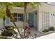 Close up of a white home's front entrance, featuring a blue door, palm trees and lush tropical foliage at 9639 Mainlands E Blvd, Pinellas Park, FL 33782