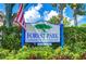 Community sign for Forest Park Condominium Association with American flag and lush landscaping at 2139 Elm St # 308, Dunedin, FL 34698