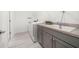 Well-lit laundry room with gray cabinets, sink, modern washer and dryer, and durable tile flooring at 5547 Silver Sun Dr, Apollo Beach, FL 33572