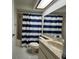 Well-lit bathroom featuring a vanity with sink, toilet, and shower with a stylish blue and white striped curtain at 946 Madrid Dr, Palm Harbor, FL 34684