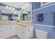 Well-lit blue bathroom featuring double sinks, a wide mirror, and classic white cabinetry at 80 Sycamore Ct, Palm Harbor, FL 34683
