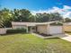 View of a single-story home with green lawn, large trees, and a two-car garage at 6521 Cedarbrook S Dr, Pinellas Park, FL 33782