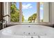 Modern standalone bathtub featuring jacuzzi jets and a bright window view of tropical greenery at 7115 Bay St, St Pete Beach, FL 33706