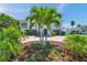Well-manicured front yard featuring palm trees and colorful flowerbeds in front of a light blue home at 7115 Bay St, St Pete Beach, FL 33706