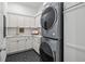 Well-lit laundry room with gray stacked washer and dryer, black hexagonal floor tiles, and white cabinets at 8913 Bernini Pl, Sarasota, FL 34240
