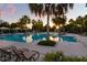 Community swimming pool lined with palm trees, lounge chairs and covered sitting areas at sunset at 11550 Lake Lucaya Dr, Riverview, FL 33579