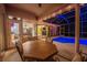Covered patio features an outdoor dining table and chairs overlooking a sparkling swimming pool at night at 1802 Oak Ridge Rd, Safety Harbor, FL 34695