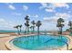 Beautiful waterfront pool with lounge chairs, blue railings, and palm trees overlooking the ocean and sandy beach at 200 1St Ave # 406, St Pete Beach, FL 33706