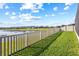 Backyard view from property, featuring green grass and a serene lake view beyond the fence at 3071 Marine Grass Dr, Wimauma, FL 33598