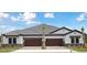 New construction duplex featuring wood garage doors, stone accents, and a tile roof under a bright sky at 35571 Stableton Ln, Zephyrhills, FL 33541