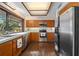 View of kitchen with stainless steel appliances, wood cabinets, brick floors, and a large window with views of the outdoor area at 14825 Lake Magdalene Cir, Tampa, FL 33613