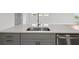 Close-up of the kitchen island featuring gray cabinets, stainless steel appliances, and a sink at 35609 Stableton Lane, Zephyrhills, FL 33541