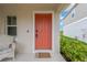 Inviting front porch with a vibrant orange door, complemented by a wicker chair and lush green shrubs at 5492 Summer Sunset Dr, Apollo Beach, FL 33572