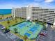 Aerial view features community tennis courts, a well-manicured lawn, palms, and ample parking, next to the condominiums at 5915 Sea Ranch Dr # 202, Hudson, FL 34667