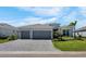 Charming single-story home with a two-car garage, paver driveway, lush green lawn, and colorful tropical landscaping at 8589 Saint Kitts Cir, Englewood, FL 34224