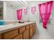 Bright bathroom featuring double sinks, wooden cabinets, and pink decorations at 2832 Brinley Dr, Trinity, FL 34655