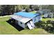Exterior view of the white home with blue roof and overgrown lawn on a sunny day at 6673 146Th N Ave, Clearwater, FL 33764