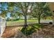 Serene backyard featuring a white fence, mature trees, and lush greenery against a backdrop of a wide-open green field at 9479 Southern Charm Cir, Brooksville, FL 34613