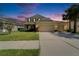 Two-story tan home with a three-car garage, manicured lawn, and palm trees at 17510 Bright Wheat Dr, Lithia, FL 33547