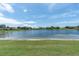 Beautiful community pond view with lush green grass in the foreground, and several houses in the background under a big blue sky at 8827 Scout Lake Ct, New Port Richey, FL 34654