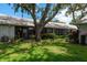 A view of the back of the home with large windows, beautiful landscaping, and a mature shade tree at 1065 Tartan Dr # C, Palm Harbor, FL 34684