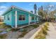 Side view of a turquoise home featuring a long covered porch, white support columns, and lush greenery at 410 73Rd Ave, St Pete Beach, FL 33706