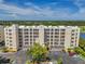 Aerial of a multistory condo building with balconies, trees, and parking in sunny weather at 1200 Country Club Dr # 6302, Largo, FL 33771