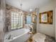 Luxurious bathroom with marble tiling, a bathtub, and a separate shower, lit by an elegant chandelier at 18003 Arbor Crest Dr, Tampa, FL 33647
