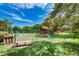 Community playground with a slide, a playhouse and a bench, nestled among lush greenery and a tennis court at 2706 11Th Ct, Palm Harbor, FL 34684