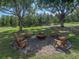 An outdoor fire pit sitting area with wooden Adirondack chairs surrounded by trees in a lush green lawn at 16326 Kalli Way, Dade City, FL 33523