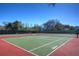 Outdoor tennis court featuring a green and red surface, surrounded by lush trees and a fence at 17917 Clear Lake Dr, Lutz, FL 33548