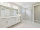 Bright bathroom featuring double sinks, white cabinetry, and a tiled walk-in shower with glass doors at 4709 Isonzo Way, Wesley Chapel, FL 33543