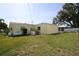 Large grassy backyard featuring a yellow house, mature trees, and a screened-in patio area at 1444 Eastfield Dr, Clearwater, FL 33764