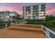 Condos with multiple balconies sit near a boardwalk with a bench at sunset at 19925 Gulf Blvd # 105, Indian Shores, FL 33785