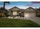 Charming single Gathering home with manicured lawn and stone accents, illuminated by landscape lighting at twilight at 7410 Ambleside Dr, Land O Lakes, FL 34637